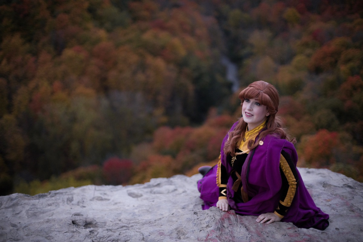 Anna is sitting on a cliff which overlooks the enchanted forest and smiling